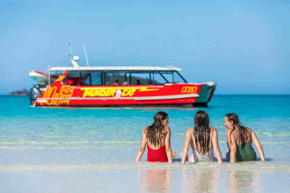 Red Cat Adventures guests waiting for snorkeling gear enjoy a red cat catamaran tour near a lush tropical island on an environmentally friendly travel experiences in paradise.
