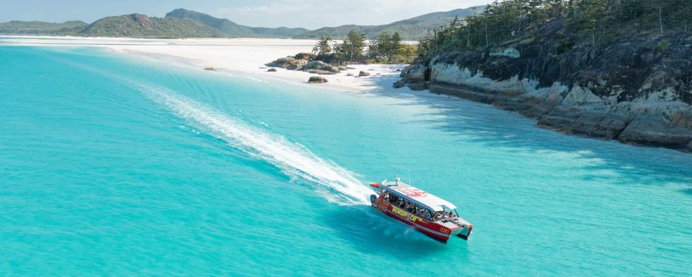 Thundercat departing Whitehaven beach going really fast across the aqua blue water leaving a lily white wake behind.