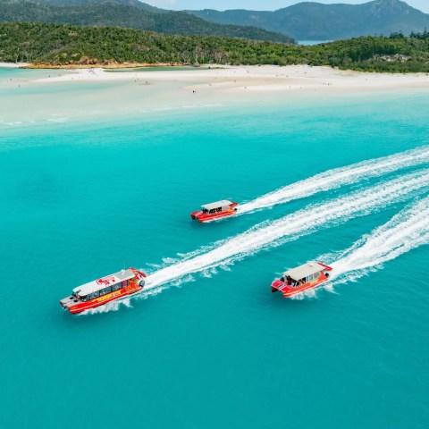 3 boats in the water infront of a beach