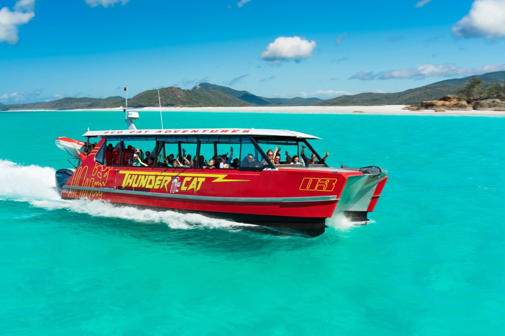 Thundercat, the Whitsundays best Boat Tour, flying through aqua blue water with the Tropical Whitsunday islands in the background and a perfect blue sky