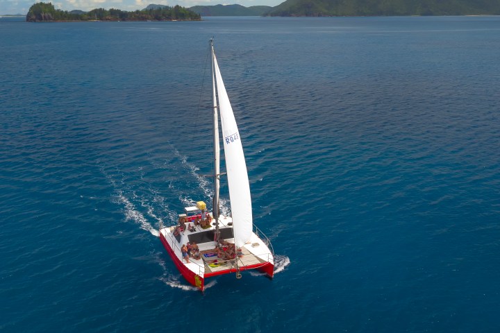 Sailboat with red trim on blue ocean, distant islands in background.