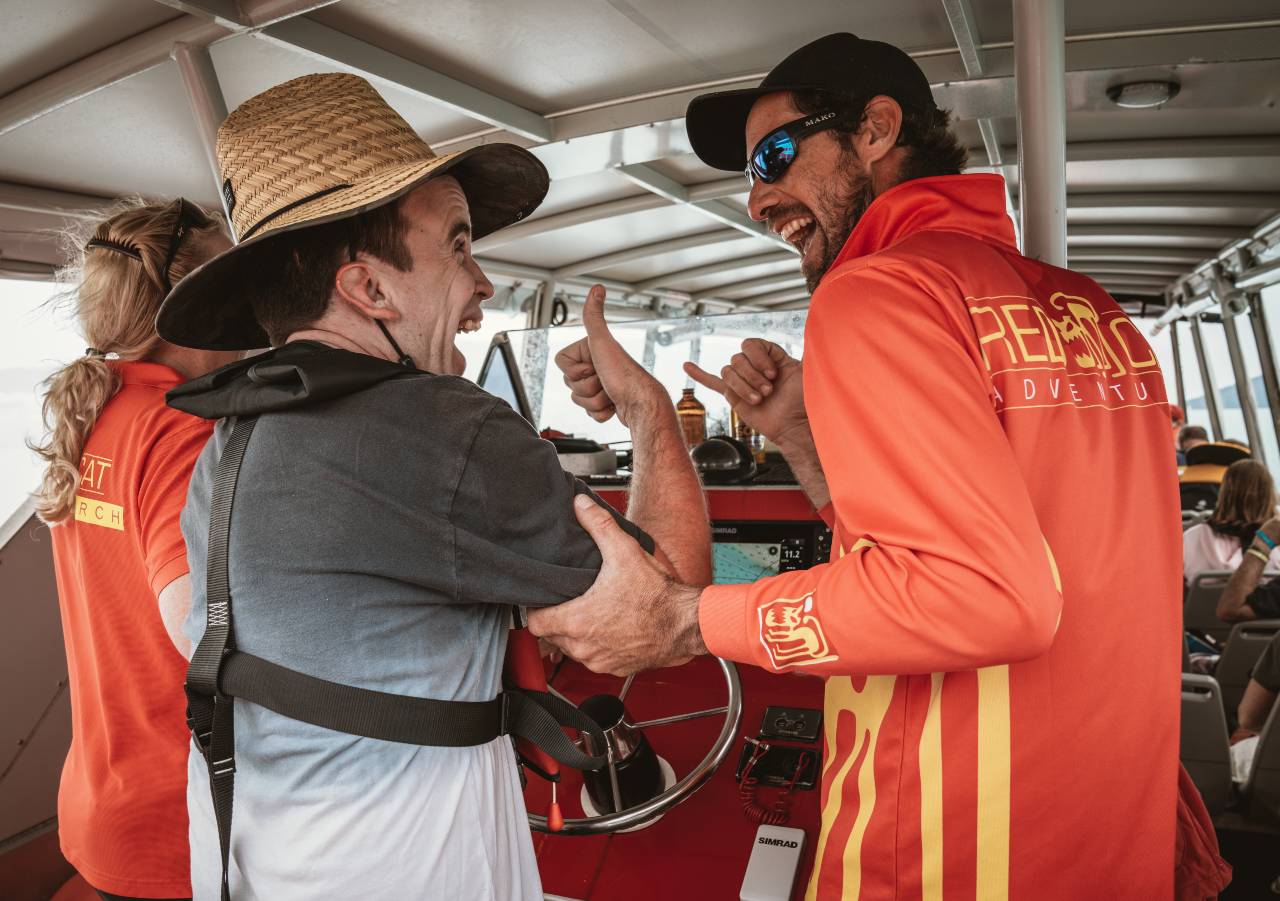 Skipper laughing with a guest on the boat who has his thumbs up laughing and enjoying the experience