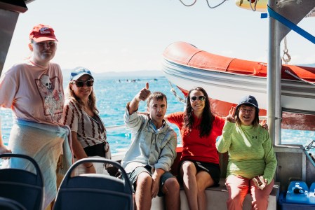 Crew member sitting on the back of the vessel with four guests giving thumbs up and smiling at the camera