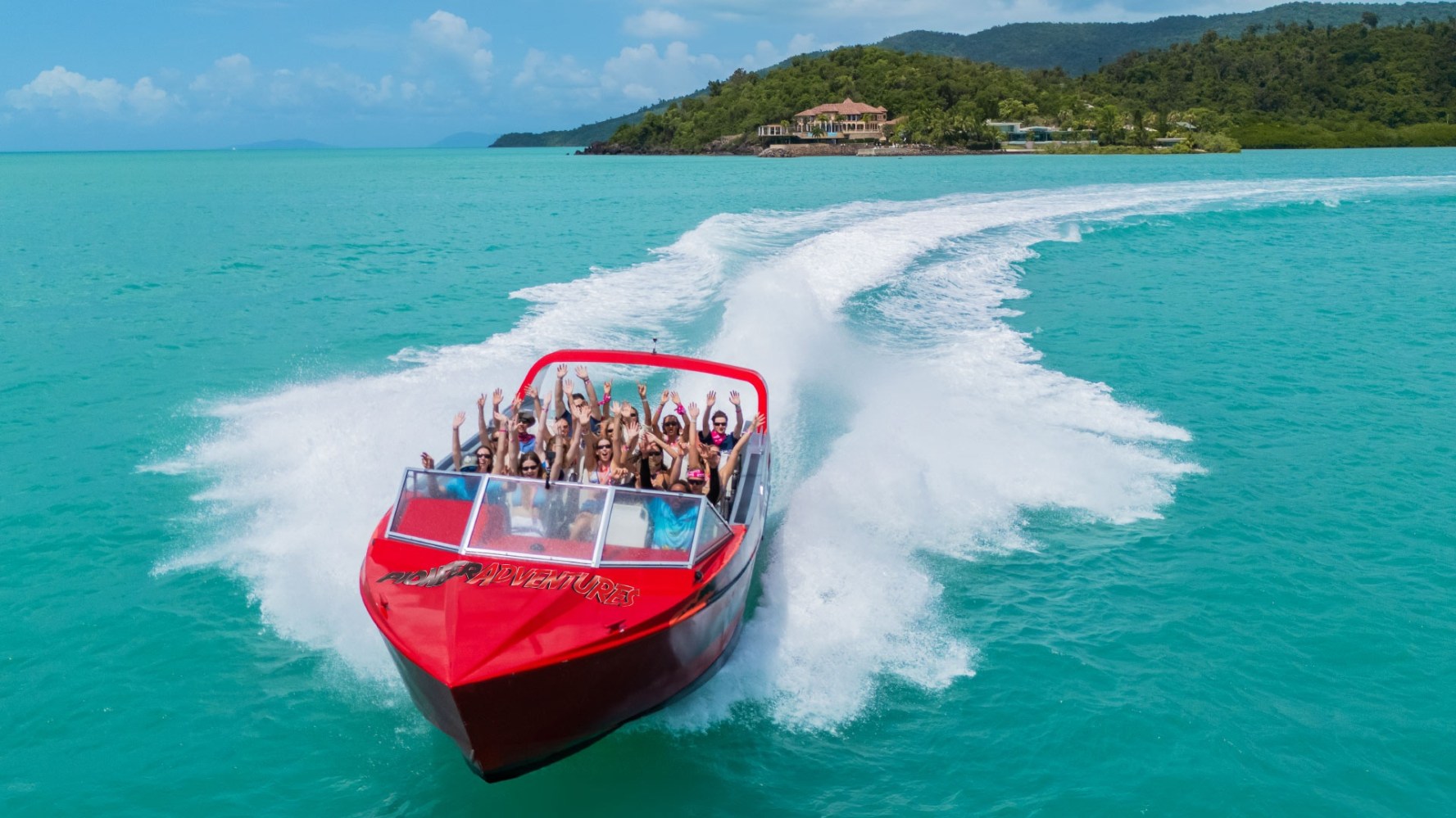 Guided boat tour in the Whitsundays with smiling adventurers on a Red Cat catamaran gliding over turquoise waters, viewing coral reefs, against lush green islands and white sand beaches under a sunlit sky. Exhilarating, scenic, and inviting freedom to explore.