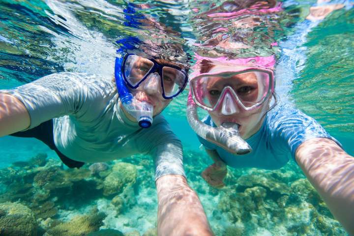 Two people snorkeling in clear water, with coral seen below them.
