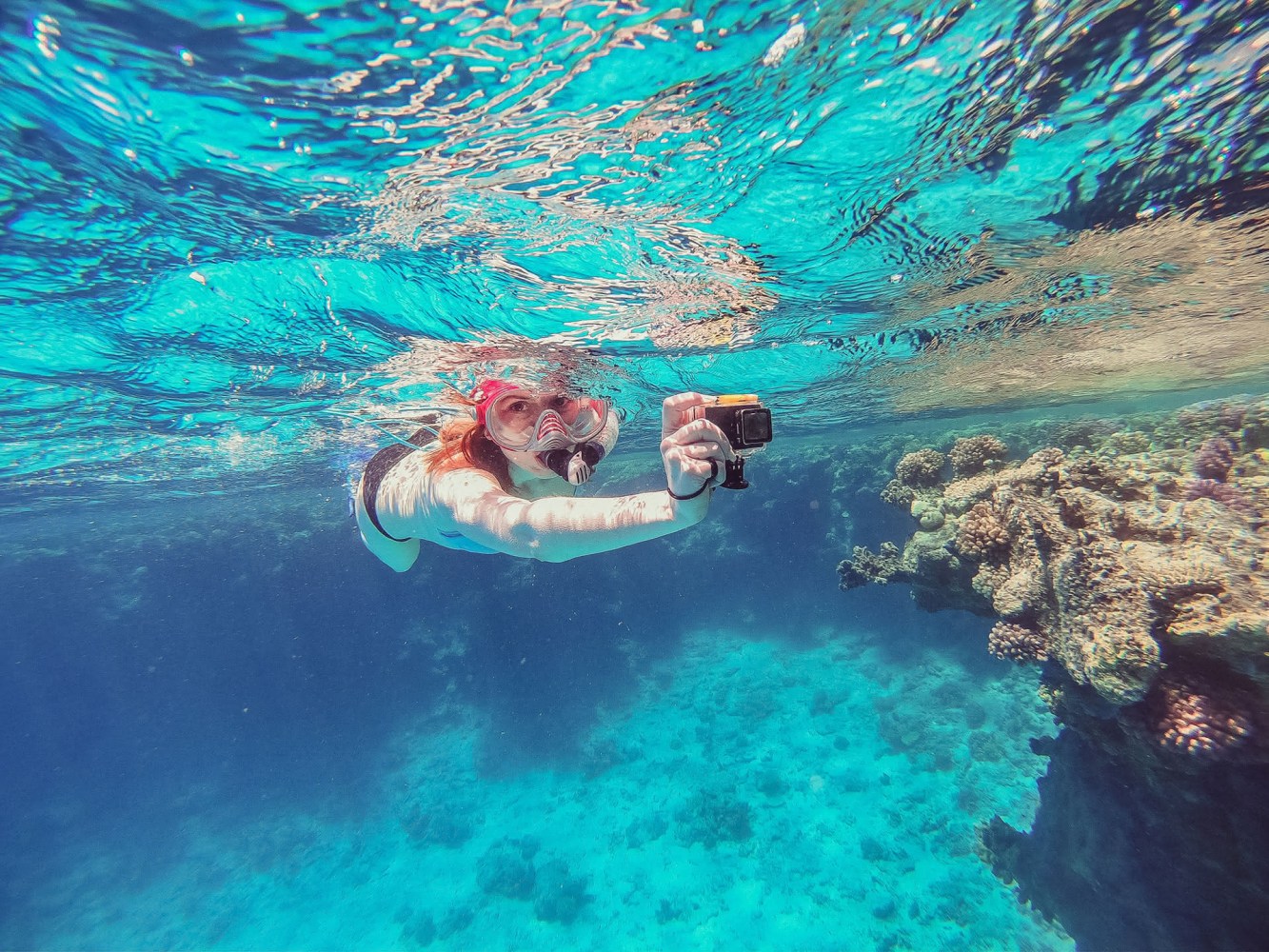 Person snorkeling underwater in the turquoise waters of the Whitsundays with an action camera near a coral bombie.