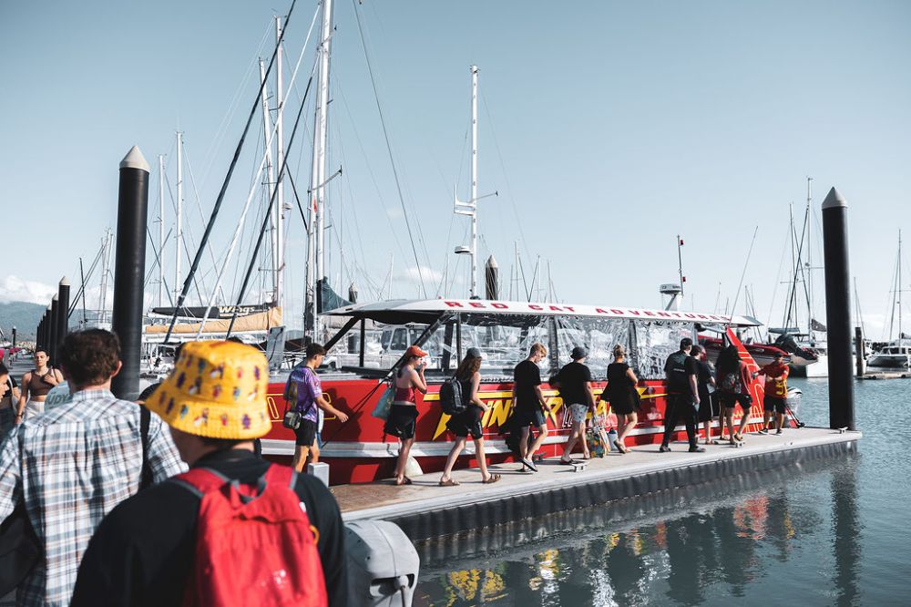 Passengers boarding Thundercat in an orderly fashion under the supervision of the Red Cat crew at the Coral Sea Marina with sailboats in the background.