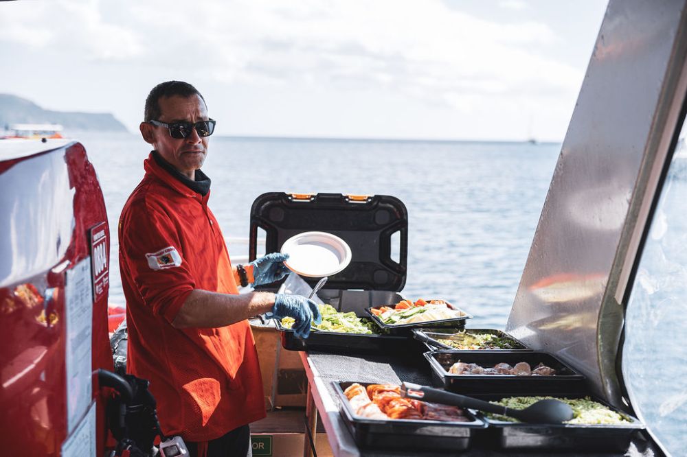 Man in red cat shirt cooking lunch onboard a Thundercat Tour waiting for the passengers who are relaxing on whitehaven beach.